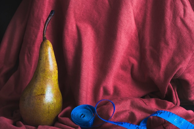 A ripe pear on a red cloth background, next to a blue measuring tape