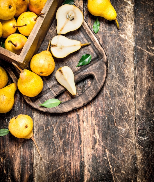 Ripe pears in a box with green leaves on rustic table.