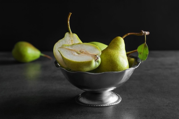 Ripe pears in metal fruit bowl on table