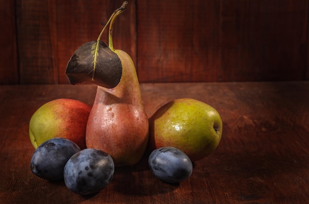 Photo ripe pears and plums on a dark wooden background in a rustic style