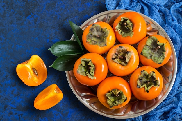 Ripe persimmon on metal plate with blue gauze napkin on textured background