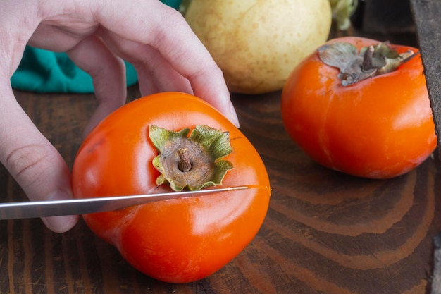 Ripe persimmon on wooden background selective focus Closeup knife in girl's hand cuts fruit