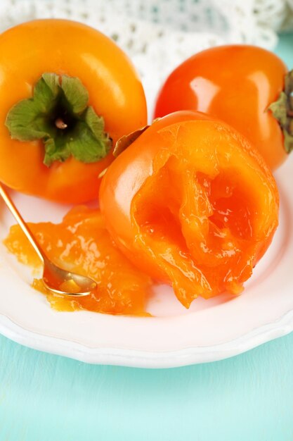 Ripe persimmons on plate on wooden background