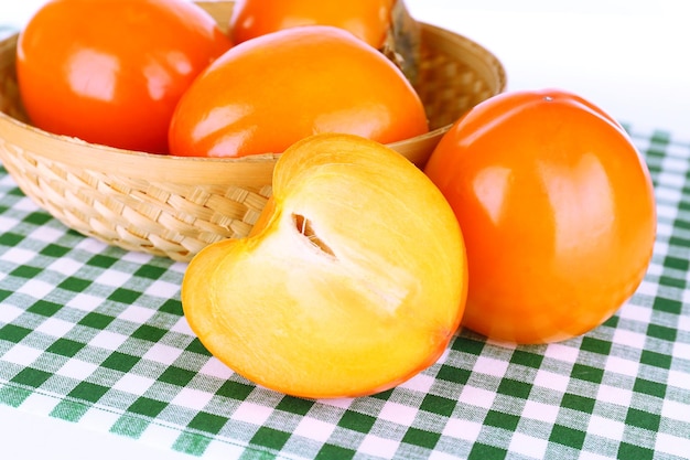 Ripe persimmons in wicker basket on table closeup