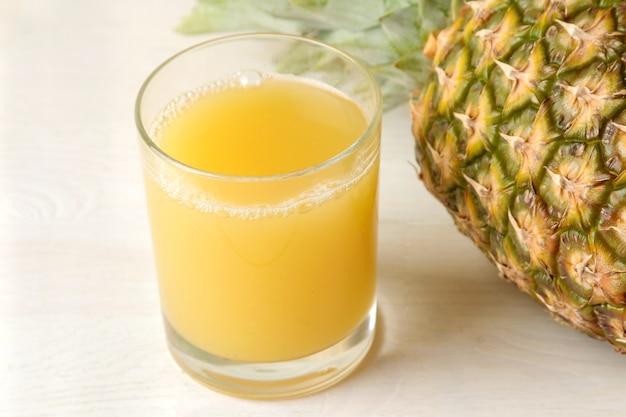 Foto frutta di ananas matura e succo di ananas su un tavolo di legno bianco. estate. avvicinamento