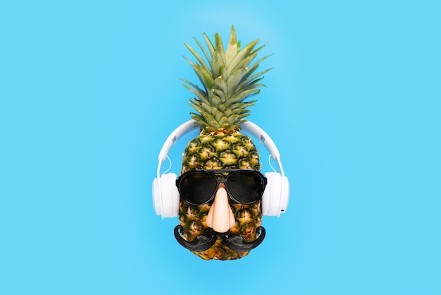 Ripe pineapple with sunglasses and headphones on blue background