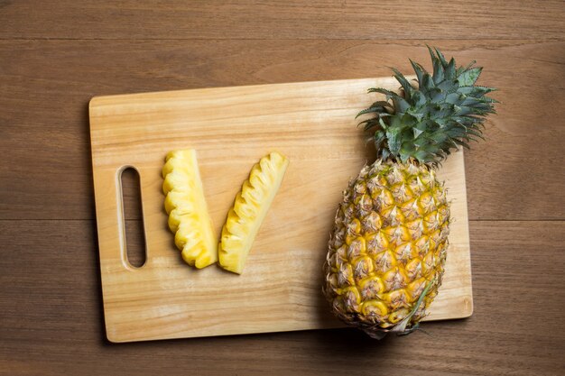 Foto ananas maturo sul tagliere di legno e sullo sfondo della tavola in legno.