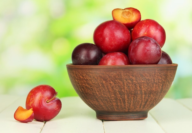 Ripe plums in bowl on wooden table on natural background