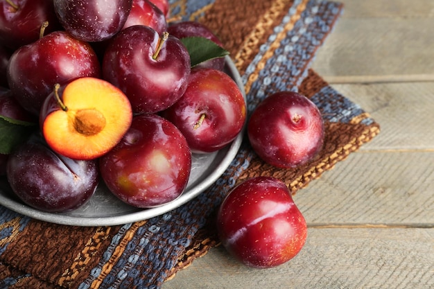 Ripe plums in metal plate on wooden table closeup