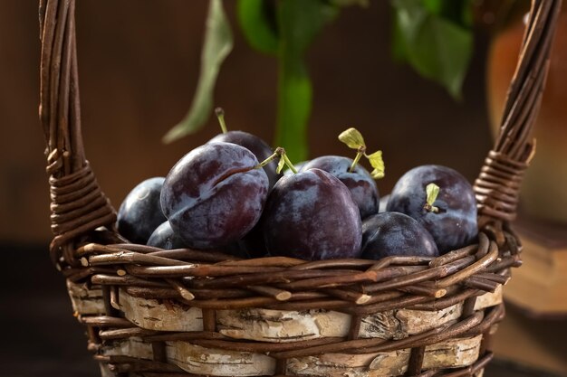 Photo ripe plums in a wicker basket on a wooden table