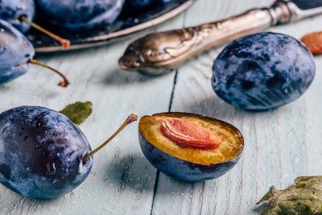 Ripe plums with sliced fruits, leaves and vintage knife over light wooden surface