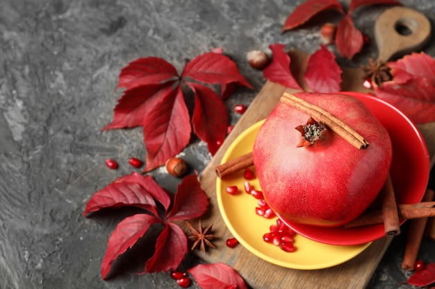 Photo ripe pomegranate, cinnamon and autumn leaves on table