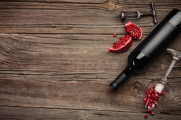 Ripe pomegranate fruit with a glass of wine, a bottle and a corkscrew on a wooden background