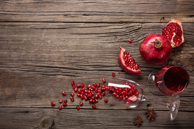 Ripe pomegranate fruit with a glass of wine and a corkscrew on a wooden background