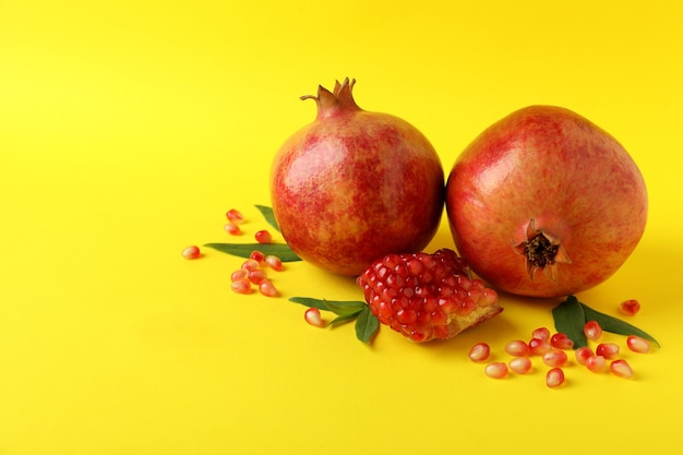 Ripe pomegranate, leaves and seeds on yellow background