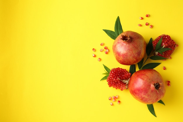 Ripe pomegranate, leaves and seeds on yellow background