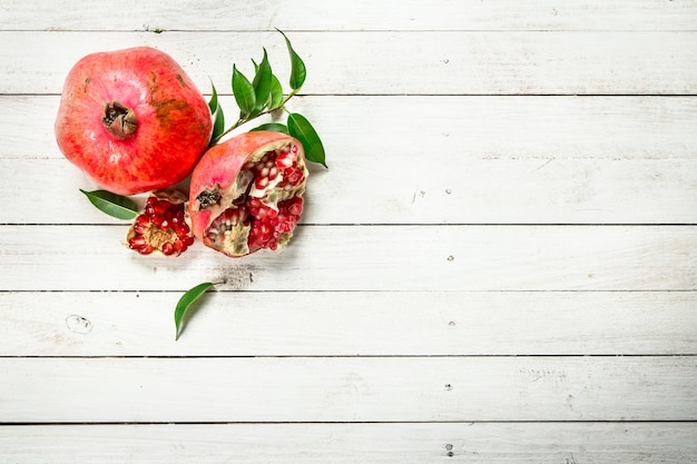 Ripe pomegranates with leaves. On a white wooden table.