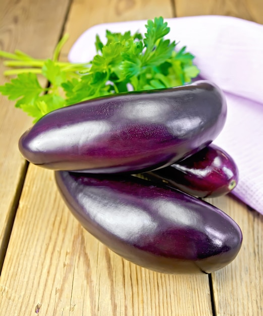ripe purple eggplants with parsley and a napkin on a wooden boards background
