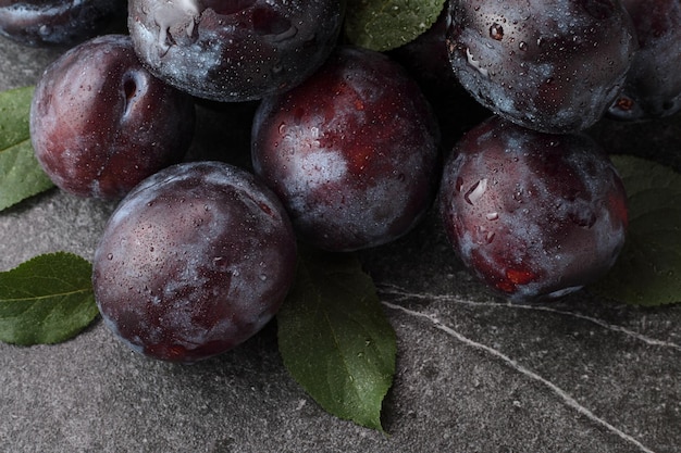 Ripe purple plums with leaves on stone table close up