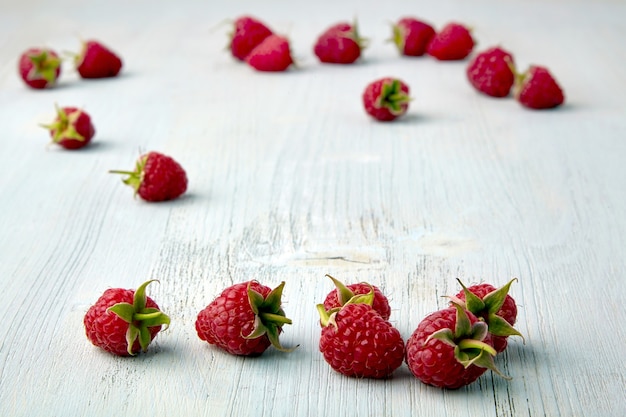 Ripe raspberries are scattered at random on a wooden table