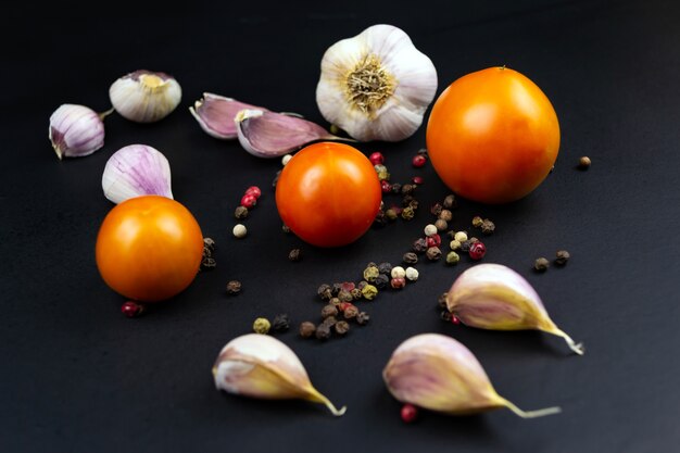 Ripe raw tomatoes, garlic on a black background.