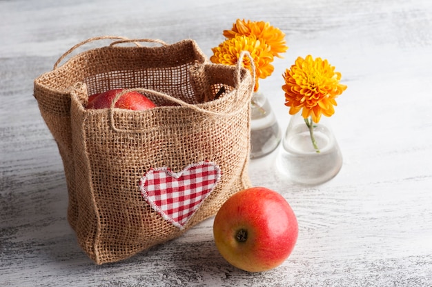 Спелые красные яблоки и сумка с сердцем на деревенском столе. Осенняя сыроедение