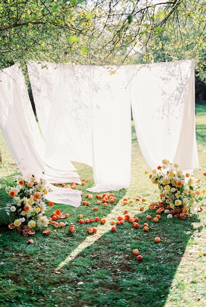 Ripe red apples and bouquets of flowers on green grass near white curtains