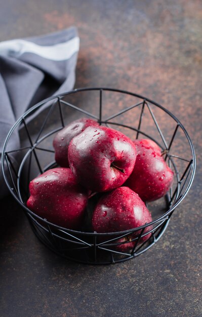 Спелые красные яблоки в металлической корзине на темном фоне таблицы. Концепция здорового питания фруктов. Копировать пространство