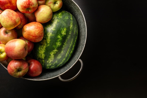 Ripe red apples and watermelon in washtub on dark background top view