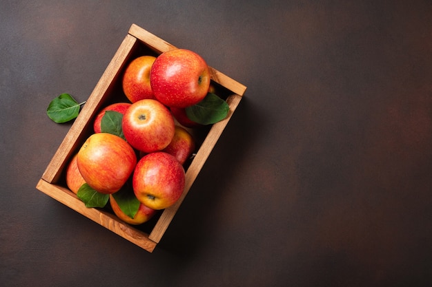 Ripe red apples in wooden box on a rusty background. Top view with space for your text.