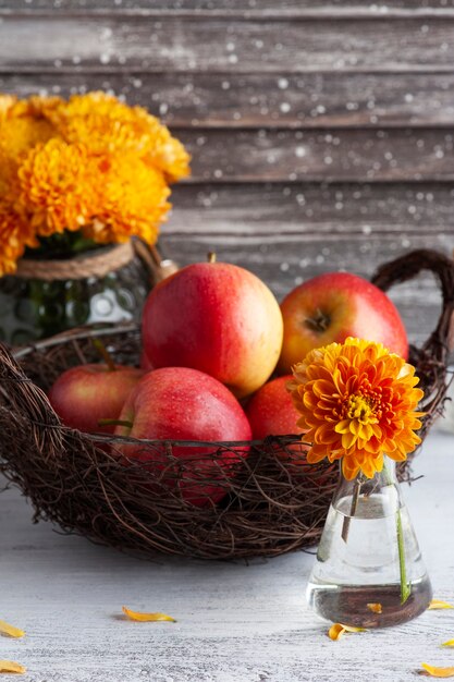 Спелые красные яблоки и желтые хризантемы на деревенском столе