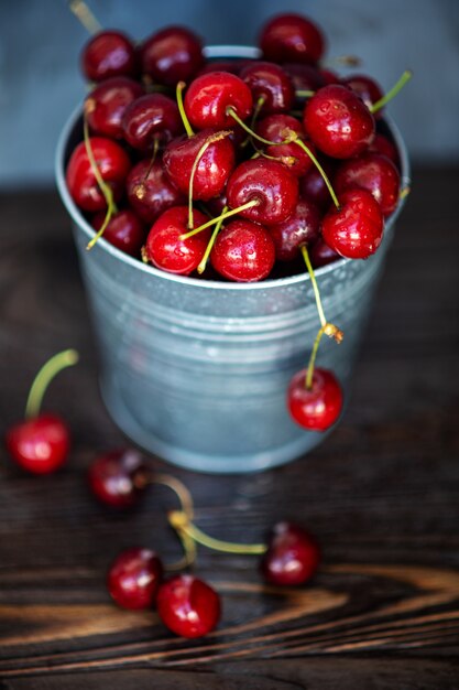 Ripe red cherries in a tin bucket on a wooden background