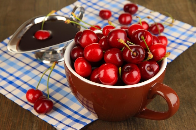 Ripe red cherry berries in cup and chocolate sauce on wooden table closeup