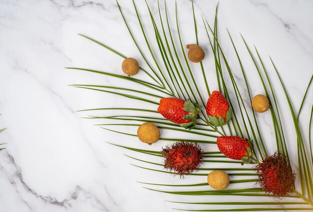 Ripe red fresh strawberries, longan fruits and green tropical leaf isolated on soft pink background. Copy space for your text. Summer, travel concept. Flat lay, top view.