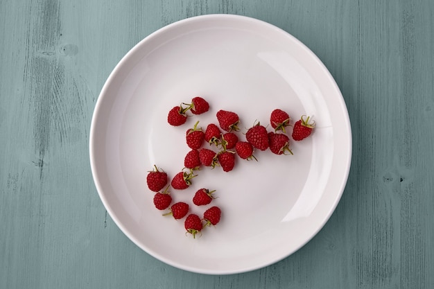 Фото Спелая красная садовая малина, разбросанная на тарелке