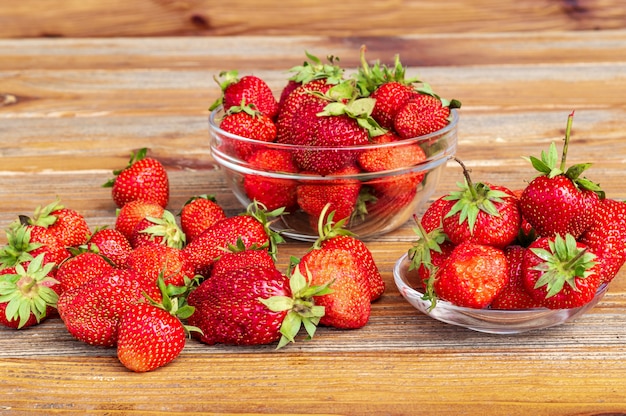 Ripe red organic strawberries in a glass bowl against brown wooden background.