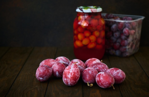 A ripe red plum and a jar of plum compote on a dark background with space for text