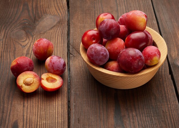 Ripe red plums in a round wooden plate on the table