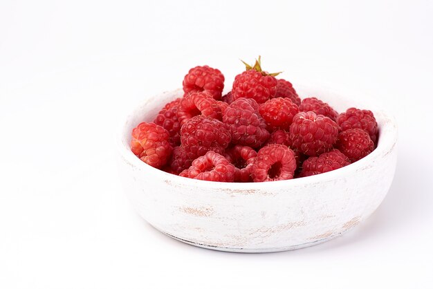 Ripe red raspberries in a wooden white plate on a white background