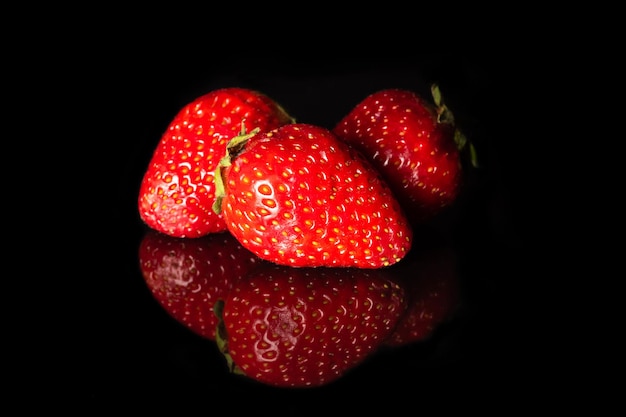 Ripe red strawberries on a black background with reflection