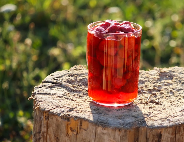 Ripe red strawberries in a glass jar on a tree stump