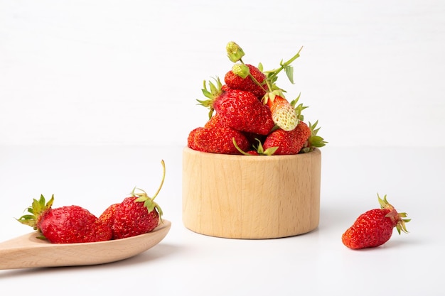 Ripe red strawberries in a spoon and cup on a white background