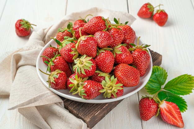 Ripe red strawberries in a white plate on a light background