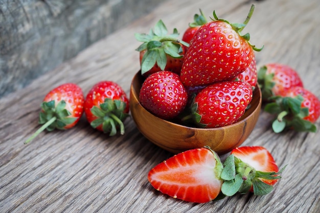 Ripe red strawberries in wood bowl on old wooden table background