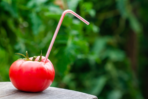 Ripe red tomato with straw on wooden surface 