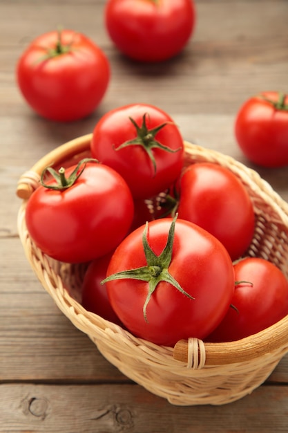 Ripe red tomatoes in a basket on grey wooden background