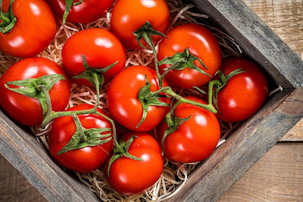 Ripe Red tomatoes in wooden market box. Wooden background. Top view.