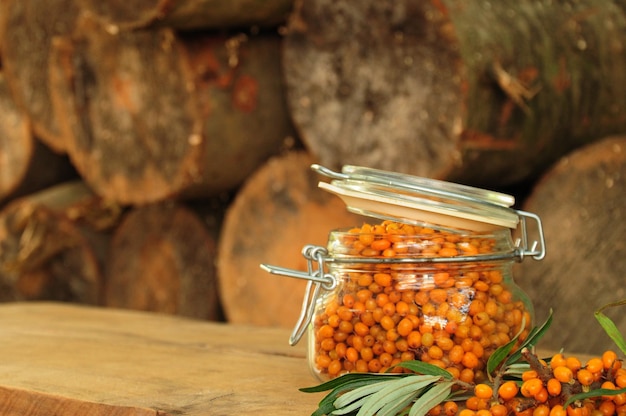 Ripe sea buckthorn berries with green leaves in a glass jar. Selective focus