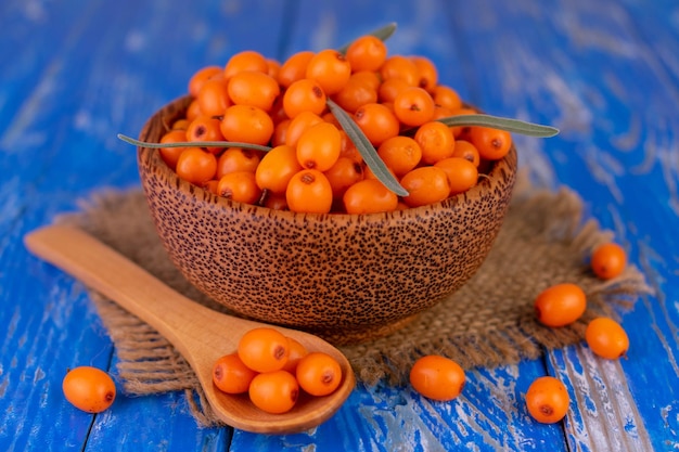 Ripe sea buckthorn in a wooden bowl on a blue background.