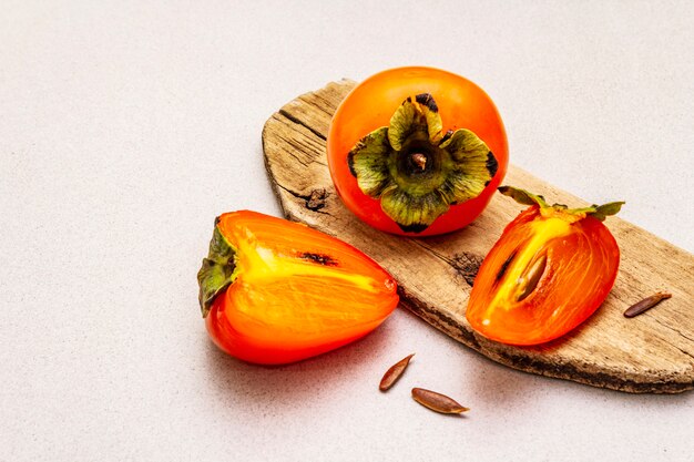 Ripe single persimmon. Fresh whole fruit, half sliced, seeds. Wooden cutting board,